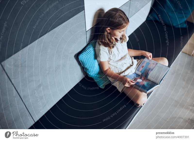 Schoolgirl reading book in school library. Primary school pupil is engaged in book. Child doing homework. Smart girl learning from book. Child curiosity back