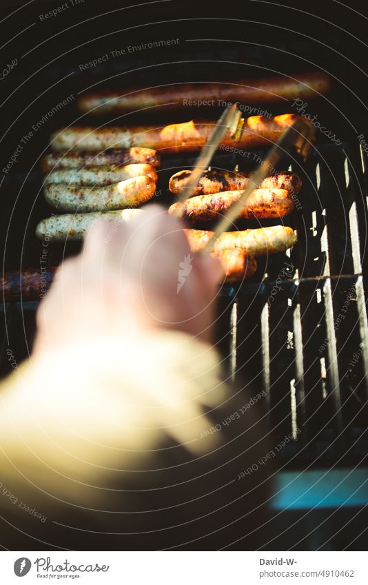 Man with barbecue tongs in hand at grill BBQ Barbecue (apparatus) grilled meat Hand BBQ season Small sausage Meat Summer