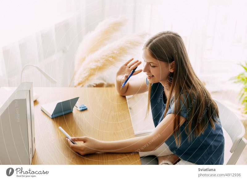 A smiling student girl is talking via video link, waving at the camera, greeting her friends or classmates chat smartphone call young videocall contact greeting