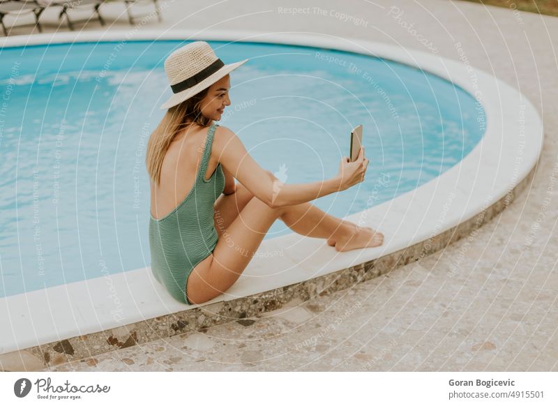 Young woman sitting by the swimming pool and taking selfie photo with  mobile phone in the house backyard bikini caucasian day enjoying exterior female fresh