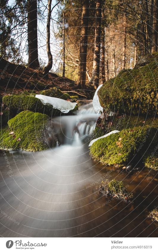 Clear water photographed with long exposure time through flowing rocks covered with moss with autumn colours of leaves. Beskydy mountains, czech republic, heart of Europe