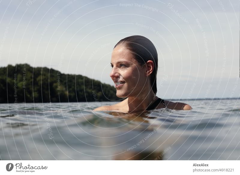 Young beautiful woman in the shallow water in the Baltic Sea looks to the side and smiles Lifestyle Back-light salubriously pretty Woman Athletic Slim Esthetic