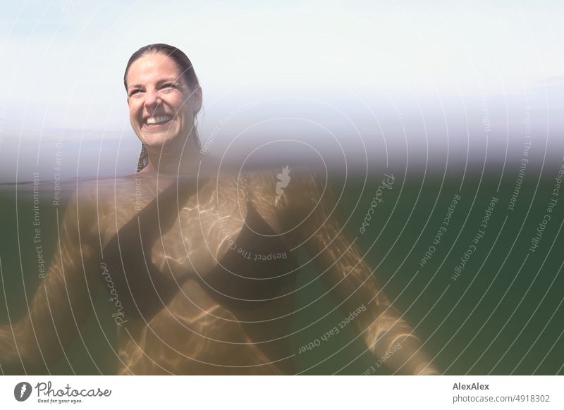 Young beautiful woman in shallow water in Baltic Sea looks to the side and smiles - visibility part- underwater picture Lifestyle Back-light salubriously pretty