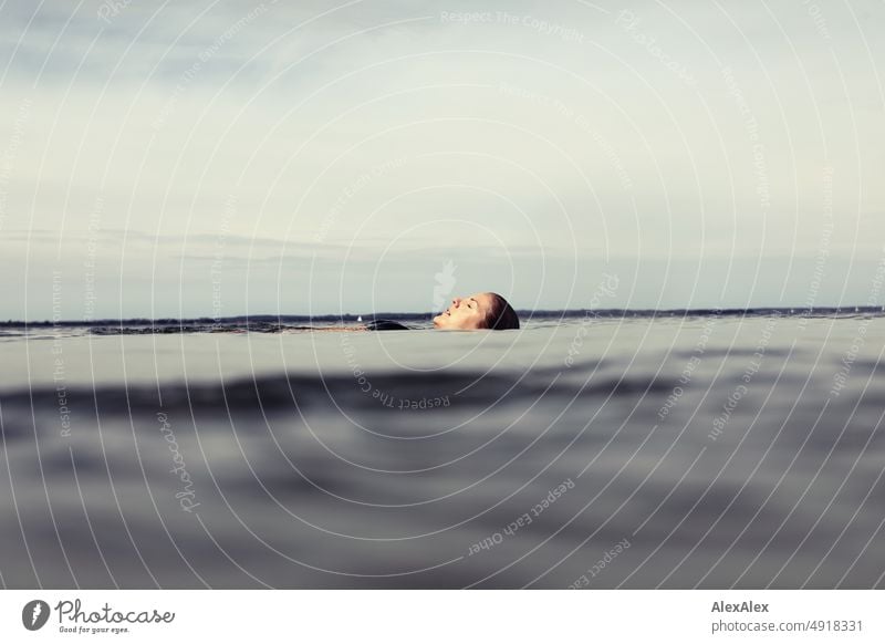 Young beautiful woman lying in the shallow water of the Baltic Sea and drifting lying on the calm sea with closed eyes Lifestyle Back-light salubriously pretty