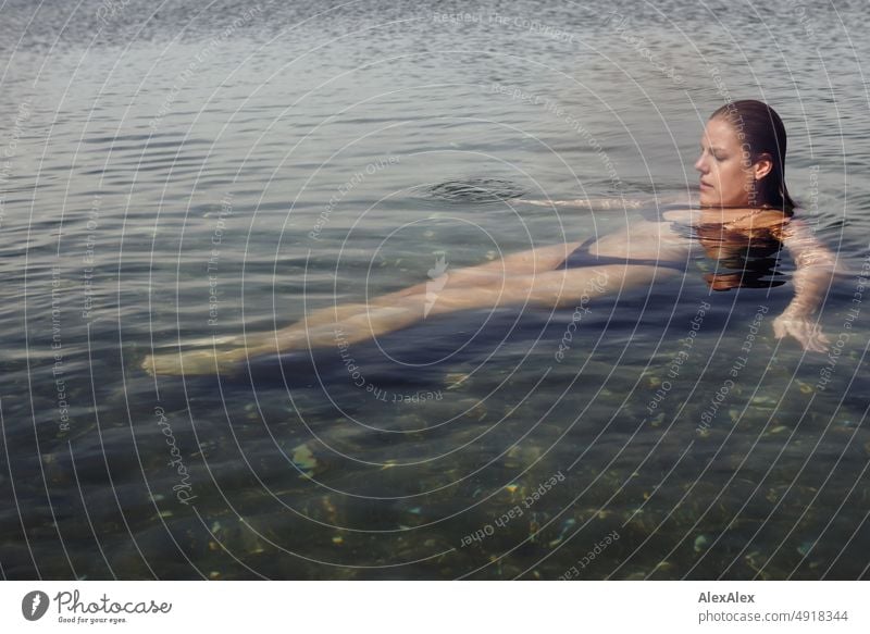 Young beautiful woman lying in the shallow water of the Baltic Sea and swimming on the calm sea Lifestyle Back-light salubriously pretty Woman Athletic Slim