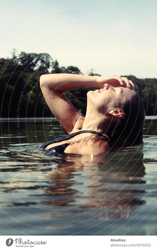 Young beautiful woman in the shallow water in the Baltic Sea smiles and strokes through her wet hair Lifestyle Back-light salubriously pretty Woman Athletic