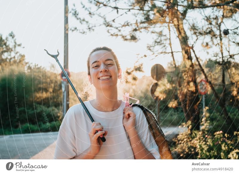 Volunteer girl cleaning the forest from pollution and plastics at sunset with garbage, smiling to camera, happy eco friendly day.Nature cleaning, ecology green concept.Environment copy space