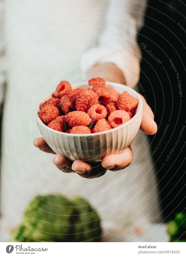 Close up image of an old woman cooking chef grabbing raspberry offering to camera before preparing them in a healthy food.Rustic cuisine cooking made by chef. Preparing ingredient for a bio meal.