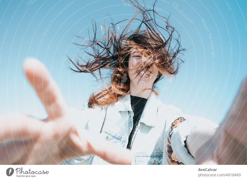 Young carefree woman on trendy modern clothes reaching to camera while doing a funny selfie while the wind moves her hair. Celebration and holiday concept. Liberty and freedom