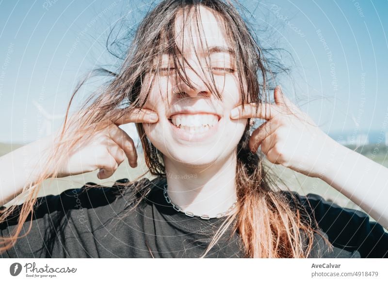 Young happy fun carefree girl smiling with big teeth to camera while pointing her dimples to camera. Bright and great future concept. Sustainable world, new generations, gen z world. Modern look.