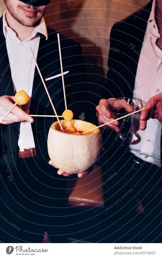 Unrecognizable men eating melon in restaurant party snack fruit friend ball celebrate occasion food festive skewer bonding elegant friendship delicious tasty