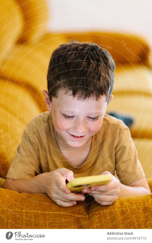 Happy boy lying on a sofa browsing on smartphone child home happy smile delight technology indoors kid young concentrated cartoon movie lifestyle childhood glad