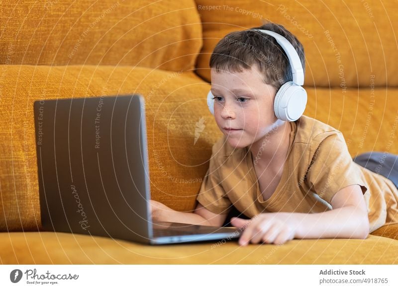 Boy sitting on a sofa with headphones on his head and using the laptop child computer boy caucasian technology male kid serious concentrate cartoon movie