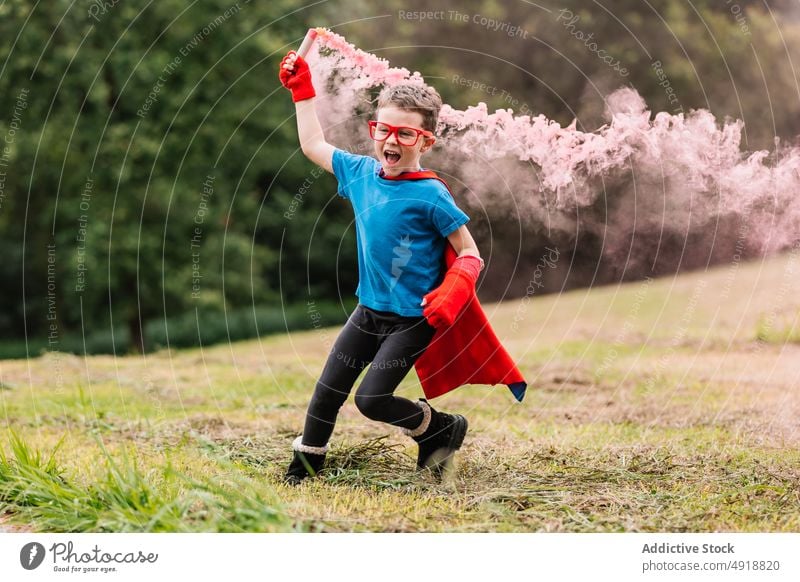 Little superhero with smoke bomb running around boy park excited costume play power lawn colorful bright smile child happy imagination fantasy adorable summer