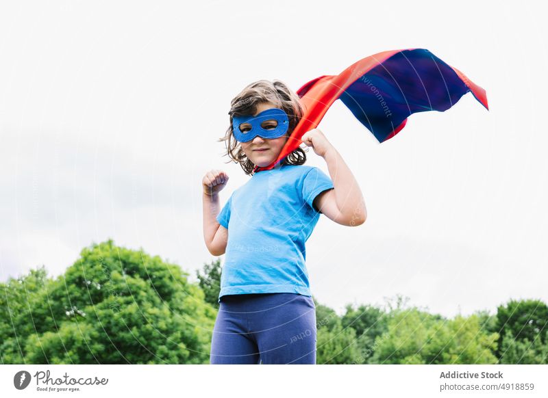 Excited girl in superhero costume in park play tree arm raised power cloudy female cape mask excited summer kid child daytime brave hand raised activity cloak