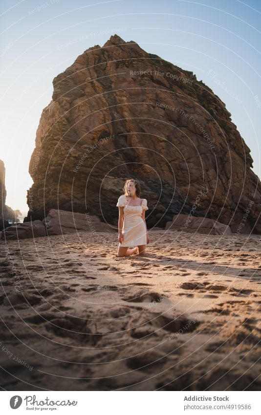 Woman sitting on beach with rock woman traveler sea water shore sunset pastime journey wanderlust stone feminine dress enjoy grace trip rest sunlight recreation