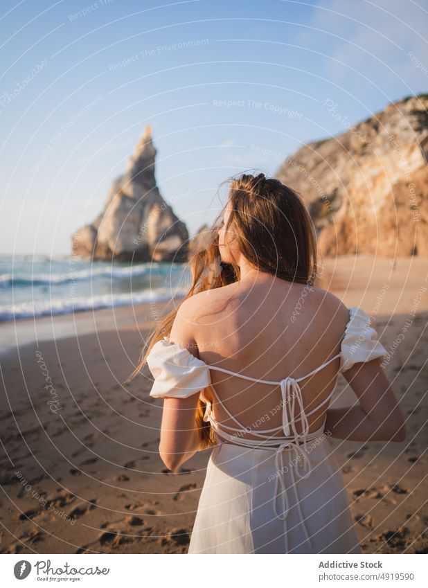 Woman standing on beach with rock woman traveler sea water shore sunset pastime journey sensitive wanderlust stone feminine dress enjoy grace trip rest sunlight