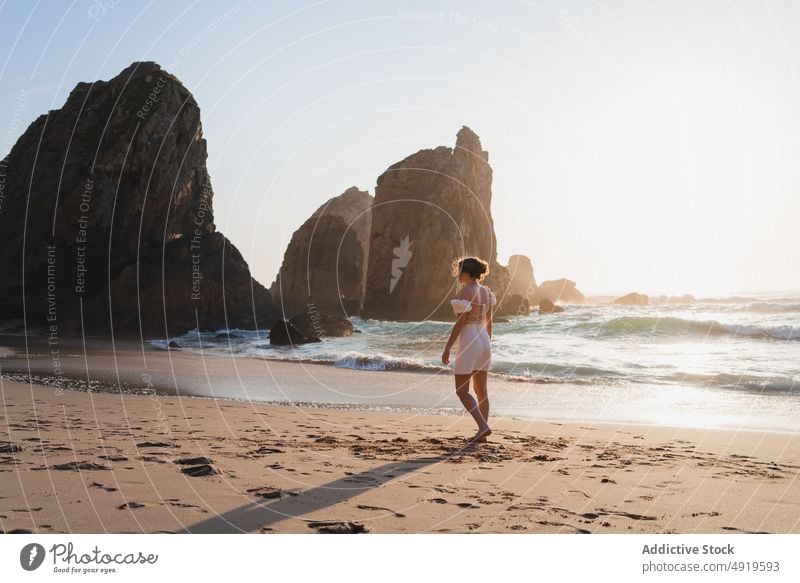 Woman walking on shore with cliffs woman traveler sea rock beach water sunset journey sunlight sundown tourist evening pastime leisure adventure active female