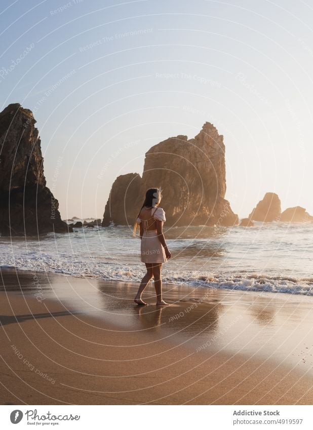 Woman walking on shore with cliffs woman traveler sea rock beach water sunset journey sunlight sundown tourist evening pastime leisure adventure active female