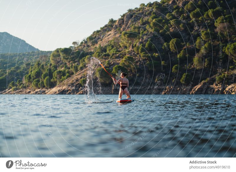 Woman floating on paddleboard in lake woman sporty surfer leisure hobby water row coast adventure sup board shore nature equipment rest rock wellbeing summer