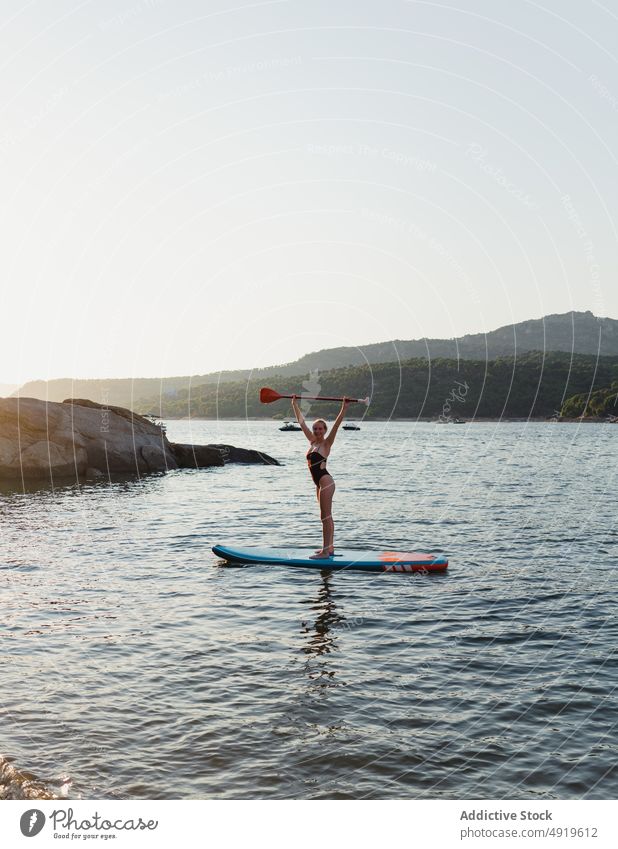 Woman in swimwear floating on paddleboard woman sporty surfer hobby lake water row practice tree coast equipment sup board adventure leisure shore nature