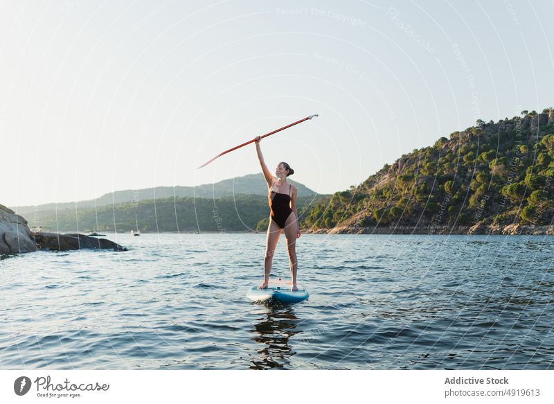 Woman in swimwear floating on paddleboard woman sporty surfer hobby lake water row practice tree coast equipment sup board adventure leisure shore nature