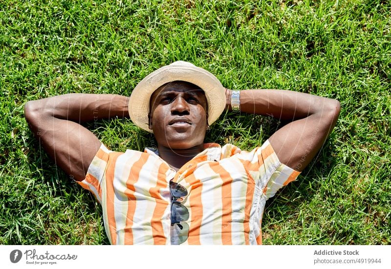 Black man lying on lawn rest relax summer field dreamy pastime park chill leisure confident african american black grass hat male ethnic casual grassy calm