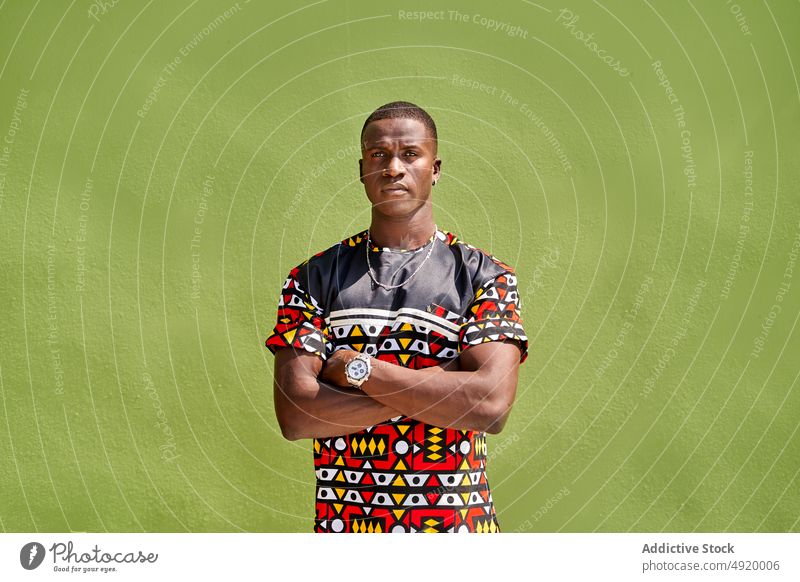 Black man standing near green wall street style city appearance serious content glad outfit fashion garment posture summer masculine african american black