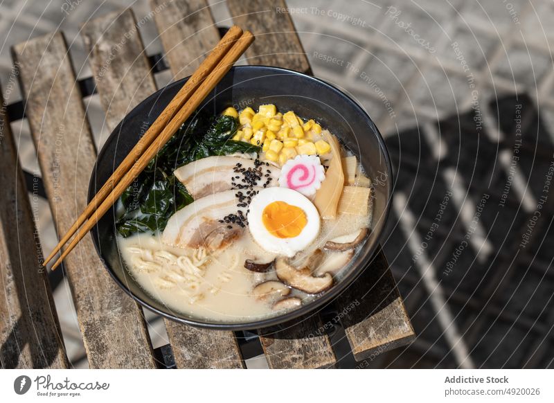 Tasty ramen served on pavement japanese noodle traditional mushroom egg culture dish street sidewalk street food ingredient broth walkway sunlight flavor meal