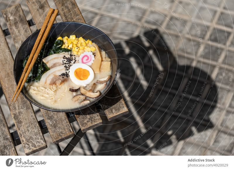 Tasty ramen served on pavement japanese noodle traditional mushroom egg culture dish street sidewalk street food ingredient broth walkway sunlight flavor meal