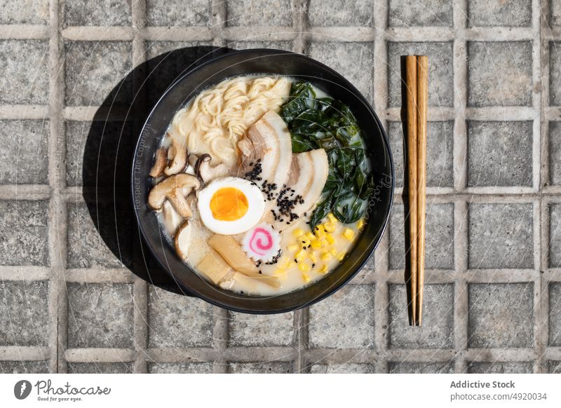 Tasty ramen served on pavement japanese noodle traditional mushroom culture dish street sidewalk street food egg ingredient broth walkway sunlight flavor meal