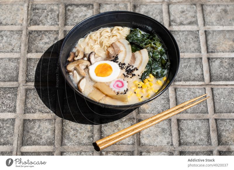 Tasty ramen served on pavement japanese noodle traditional mushroom culture dish street sidewalk street food egg ingredient broth walkway sunlight flavor meal