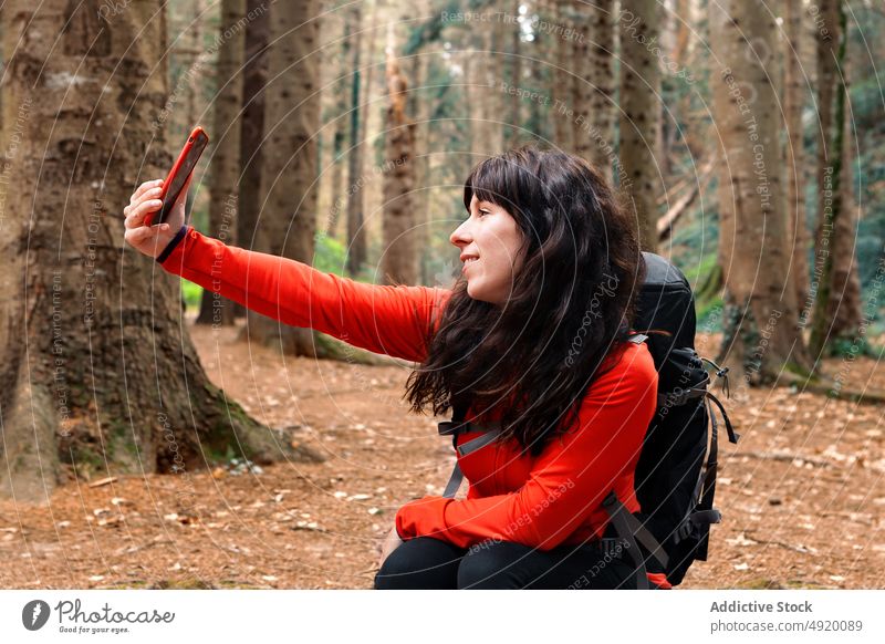 Female hiker taking selfie in forest woman smile break weekend travel smartphone female woods happy backpack self portrait glad traveler tree nature mobile