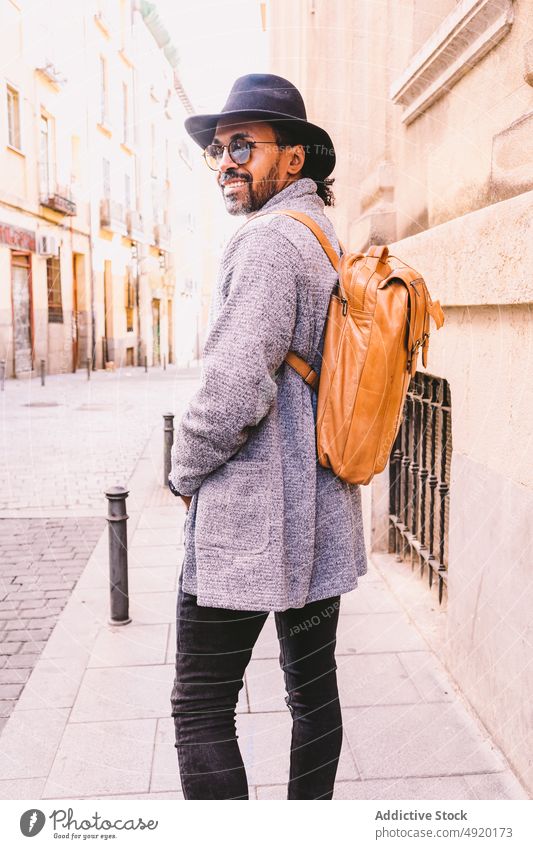 Positive trendy male on city street man walk sidewalk street style smile positive urban hand in pocket daytime adult ethnic hispanic appearance backpack