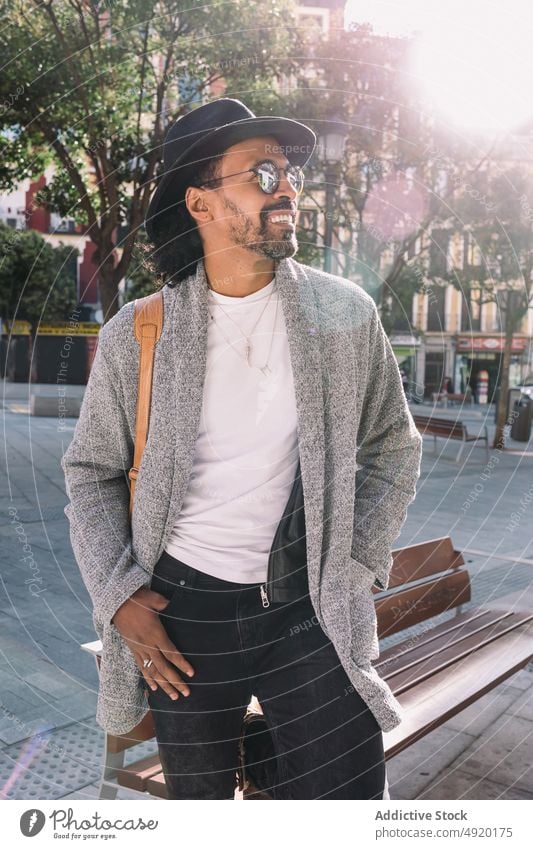 Stylish Hispanic man on city street street style urban daytime outfit sunlit bench rest appearance male hispanic ethnic adult hand in pocket modern trendy