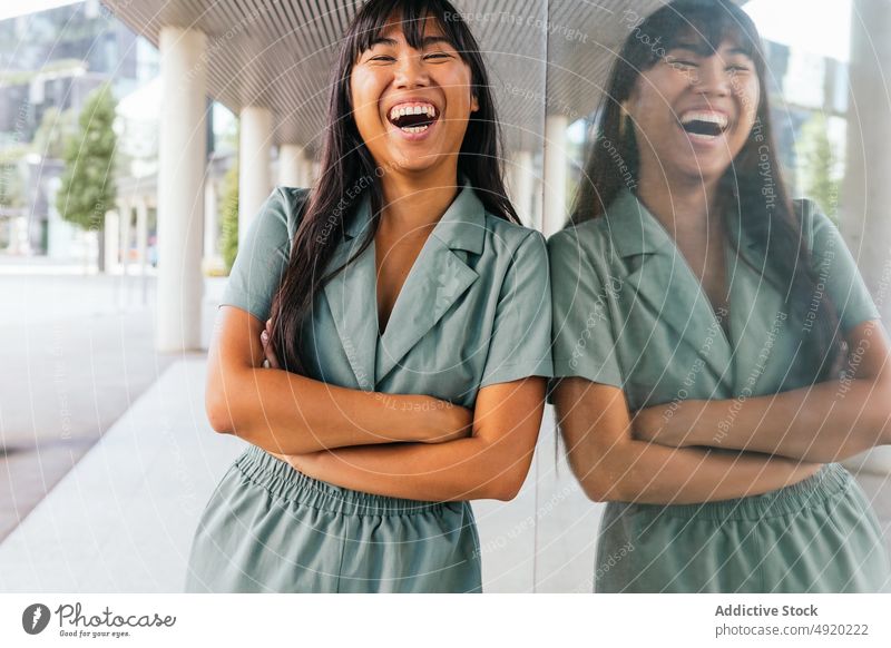 Asian female leaning on glass wall woman street rest weekend urban style appearance cheerful reflection smile young asian glad delight ethnic happy arms crossed