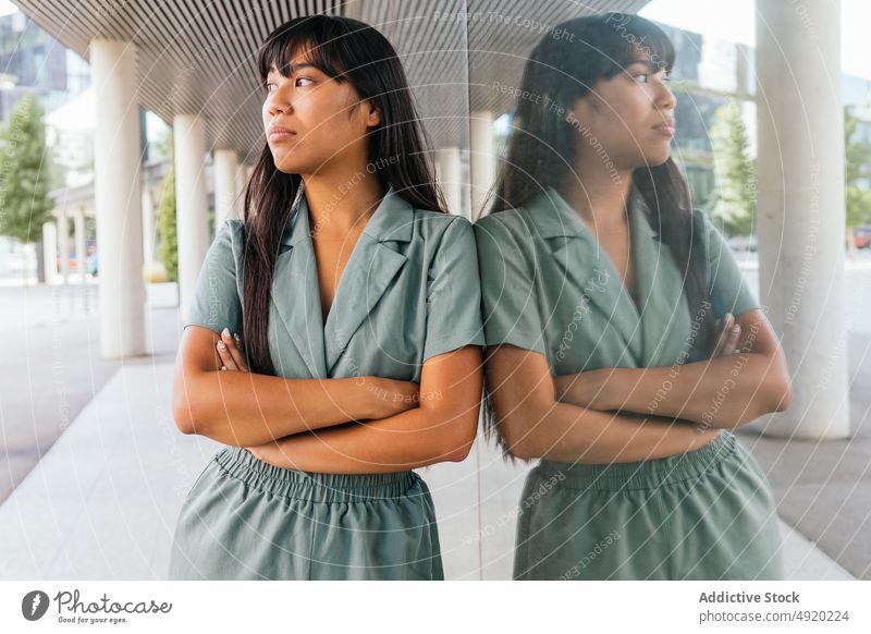 Asian female leaning on glass wall woman street rest weekend urban style appearance reflection young asian ethnic arms crossed long hair break daytime building