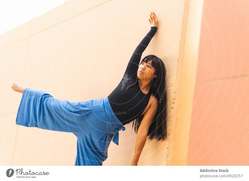 Barefoot ethnic dancer stretching on street woman flexible bend wall pavement leg raised female young asian balance building perform choreography daytime