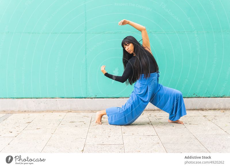 Asian woman dancing on pavement dance street grace wall arm raised lunge urban female young asian ethnic energy talent barefoot long hair black hair practice