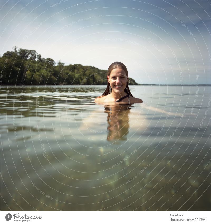 Young beautiful woman in shallow water in Baltic Sea looks at camera and smiles Lifestyle Back-light salubriously pretty Woman Athletic Slim Esthetic teen