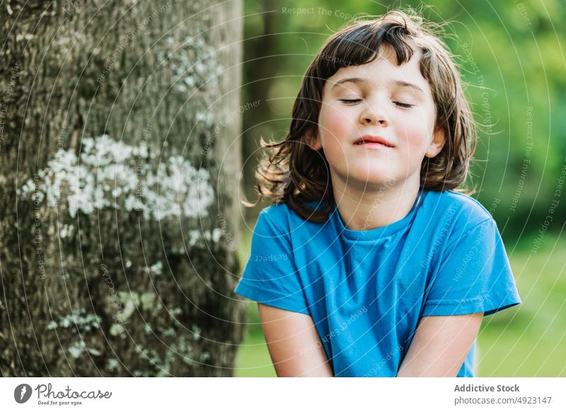 Cute little girl near tree park smile weekend summer rest trunk eyes closed portrait cute child casual t shirt dark hair adorable thoughtful childhood kid