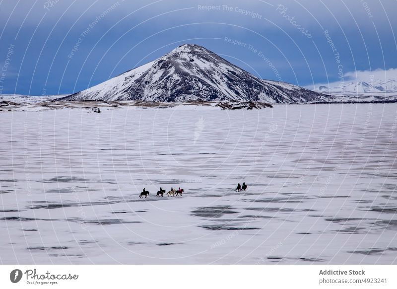 Anonymous people riding icelandic horses on snowy valley with snowy mountains travelers ride wild plain winter cold rural nature sky frost activity animal