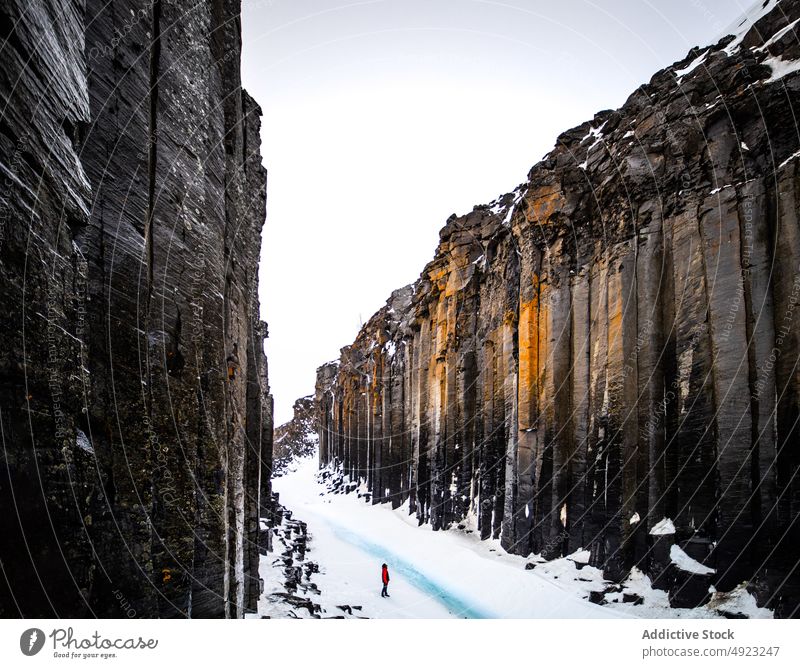 Anonymous traveler walking in between ravine and river in mountainous terrain snow landscape rock highland person scenery water rocky iceland outdoors frost