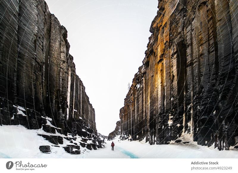 Anonymous traveler walking in between ravine and river in mountainous terrain snow landscape rock highland person scenery water rocky iceland outdoors frost