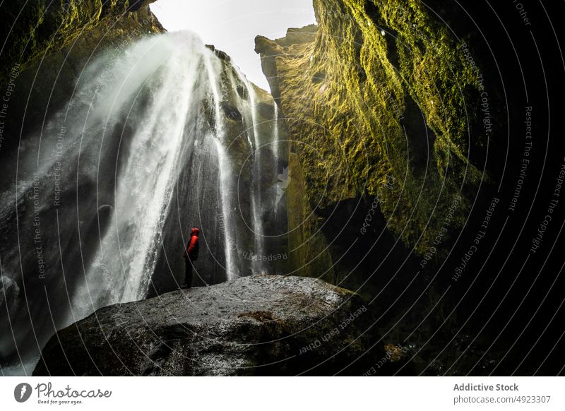 Anonymous traveler enjoying energy of powerful waterfall in rocky ravine person nature tourist admire canyon picturesque landscape cliff trip outerwear