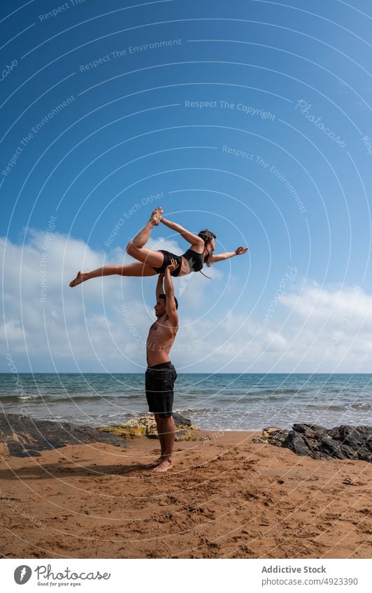 Couple doing acro yoga against cloudy sky couple beach together arms raised sea balance summer practice asana man woman energy weekend blue sky session