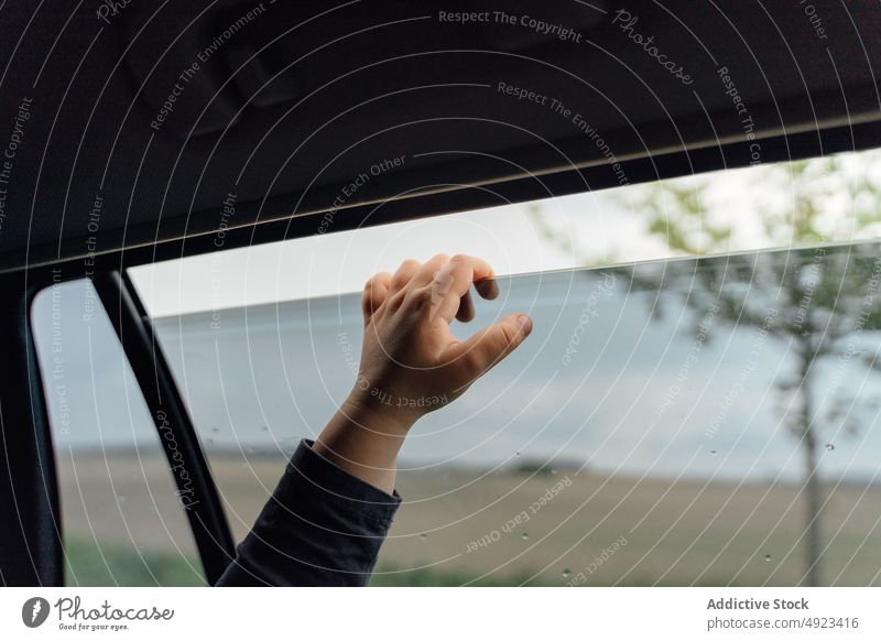 Crop child touching car window during trip road trip countryside ride admire automobile passenger vehicle journey childhood kid hand transport cloudy sky rain