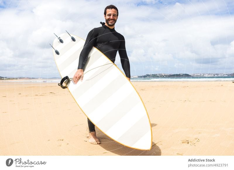 Happy young ethnic guy smiling holding surfboard on seashore man surfer beach smile shaka happy ocean athlete confident hawaiian hang loose male hispanic brunet