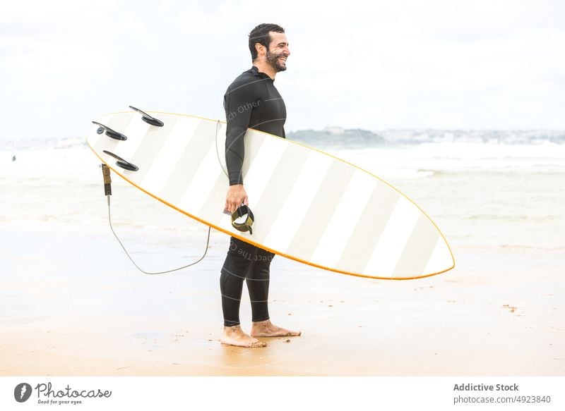 Happy young ethnic guy smiling holding surfboard on seashore man surfer beach smile happy ocean athlete confident hawaiian hang loose male hispanic brunet beard