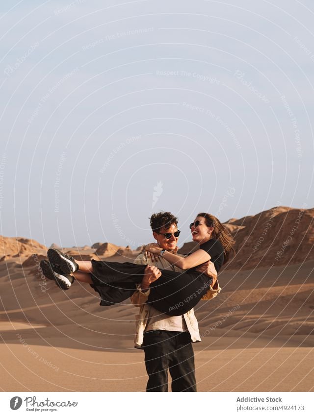 Enamored guy hugging happy girlfriend during trip in desert couple lift having fun traveler love smile relationship embrace nature beloved boyfriend young